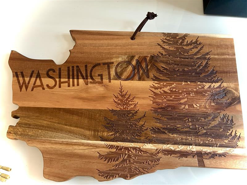 A Washington state-shaped wooden cutting board with laser-engraved trees and the word 'WASHINGTON' on a white background.